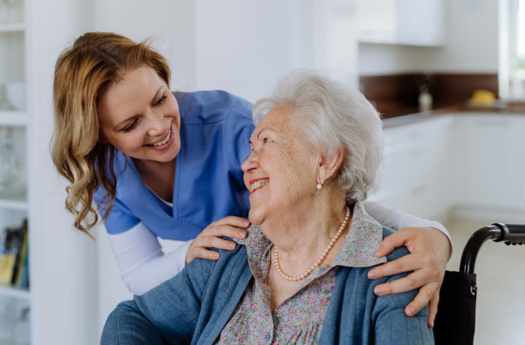 A caregiver checking in on a smiling seated resident in senior living and laughing.

