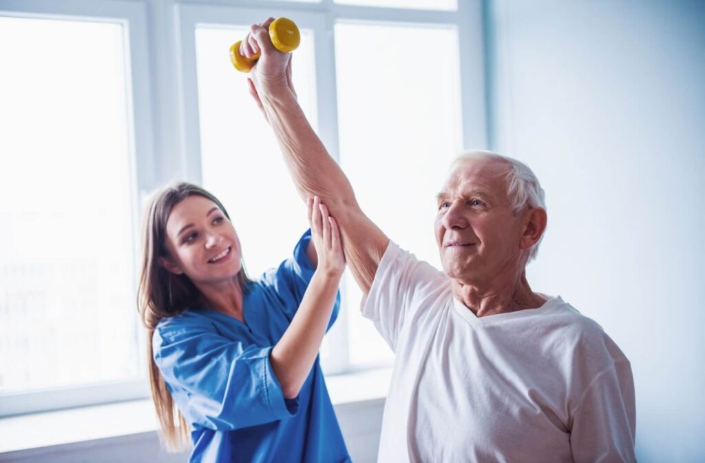 A physiotherapist in skilled nursing helps an older adult hold up a small weight with their right arm.